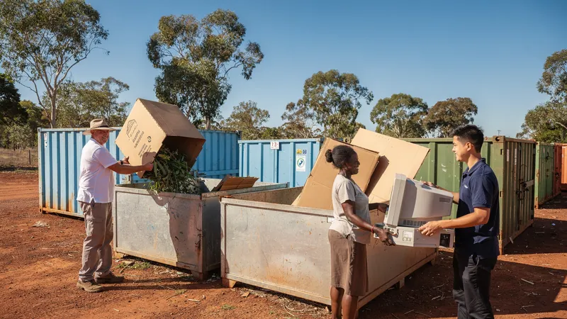 Menschen verschiedener Herkunft werfen an einem australischen Wertstoffhof Grünschnitt, Karton und einen alten Monitor in Container, Eukalyptus ringsum.